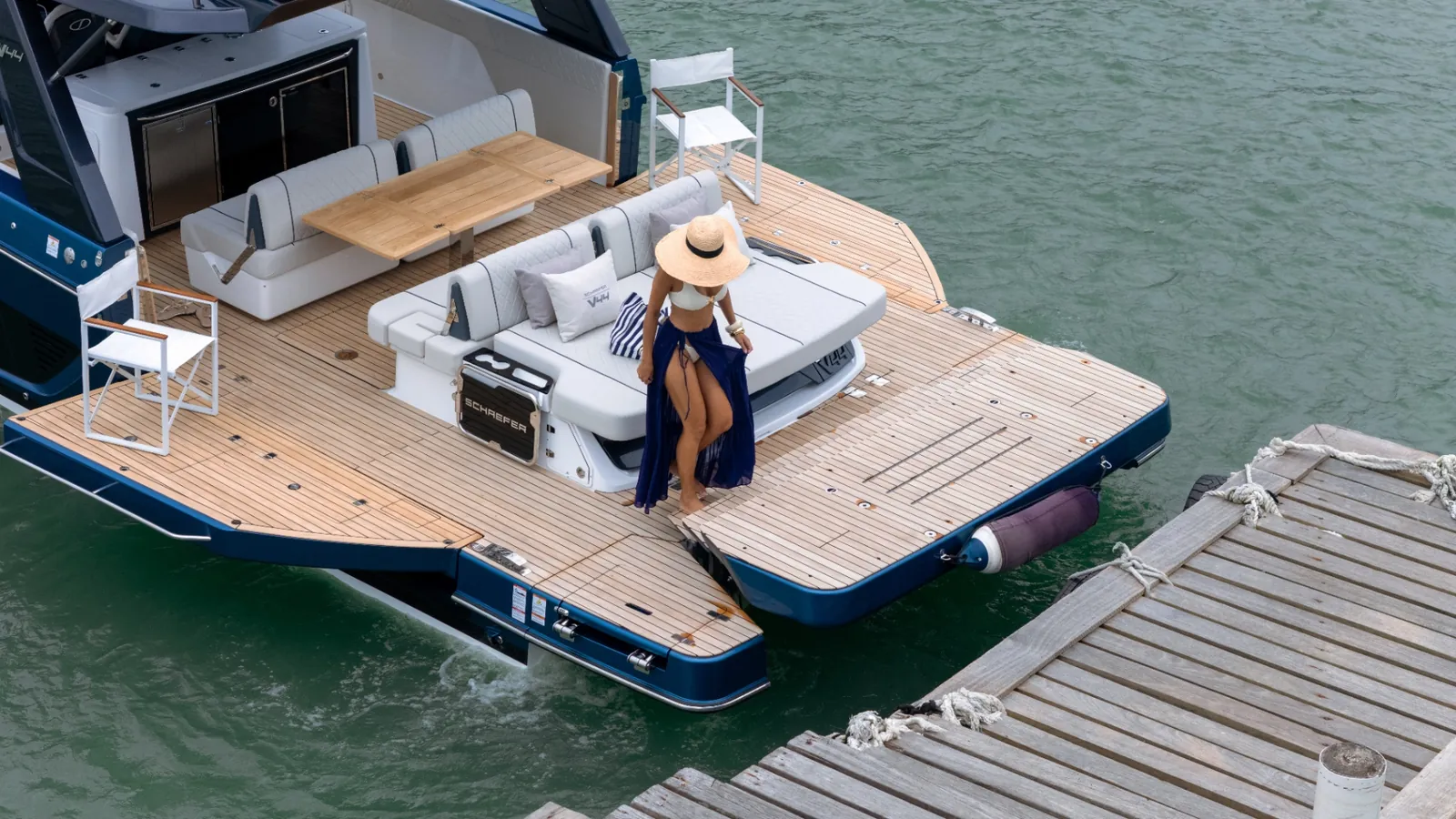 Guest on the teak aft deck of a dark-blue Schaefer V44 alongside a timber jetty, seen from above